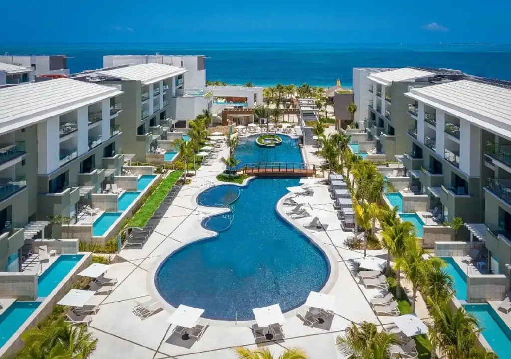 Luxurious resort featuring a stunning pool surrounded by palm trees and ocean views, ideal for relaxation and leisure.