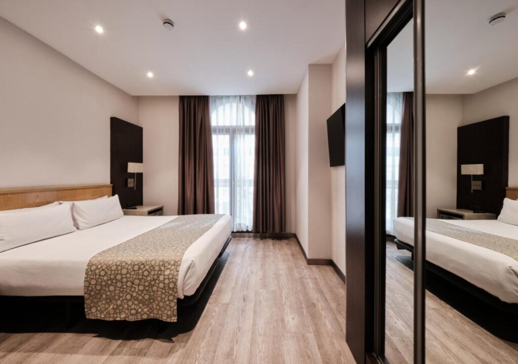 Spacious hotel room with a king-size bed, natural light, and modern decor, perfect for a relaxing stay.