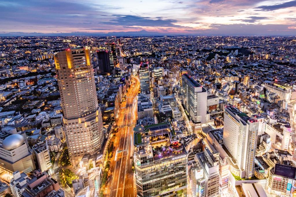 Aerial view of a vibrant urban landscape at dusk, showcasing skyscrapers and bustling city streets illuminated by lights.