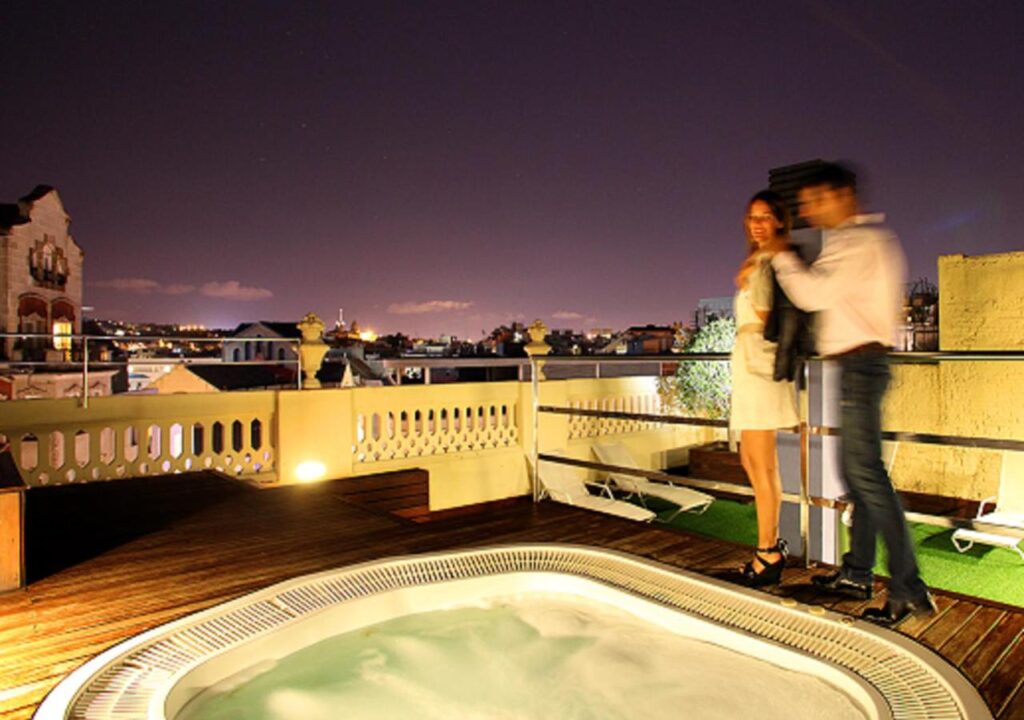 Couple enjoying a romantic evening by a hot tub on a rooftop terrace with city skyline illuminated at night.