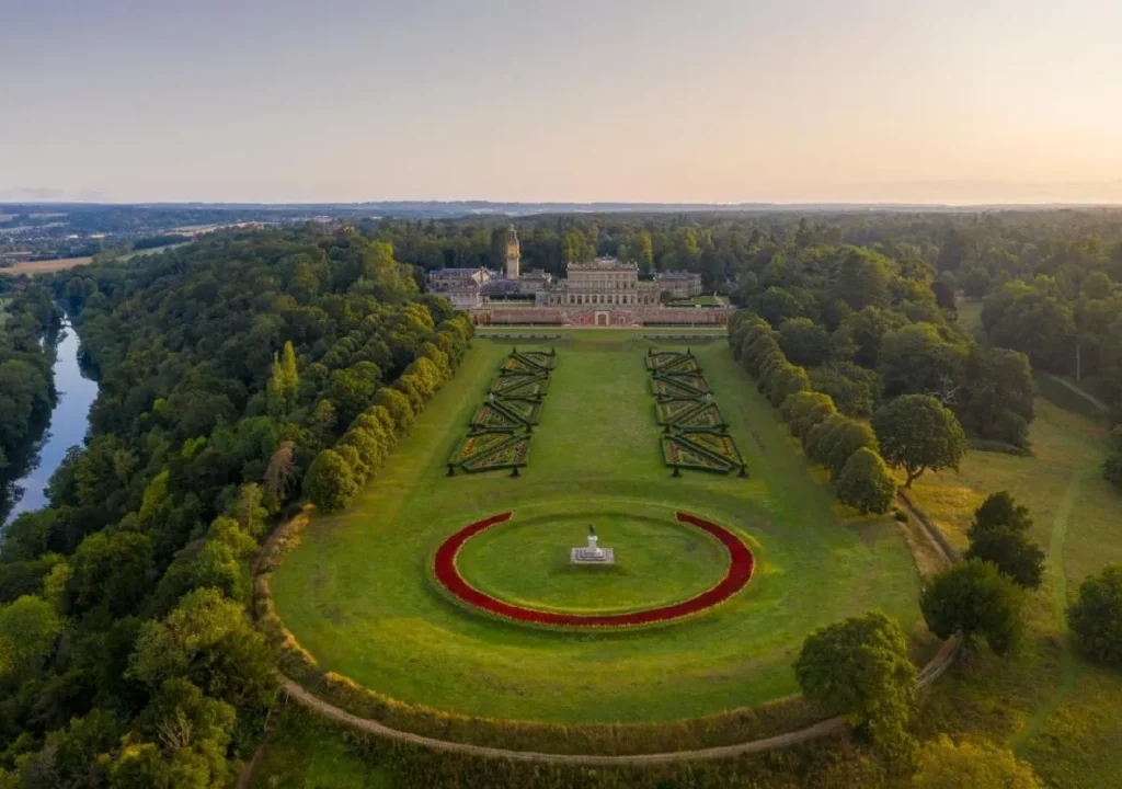 Aerial view of a grand estate with beautifully landscaped gardens and a river in the background, illuminated by sunset.