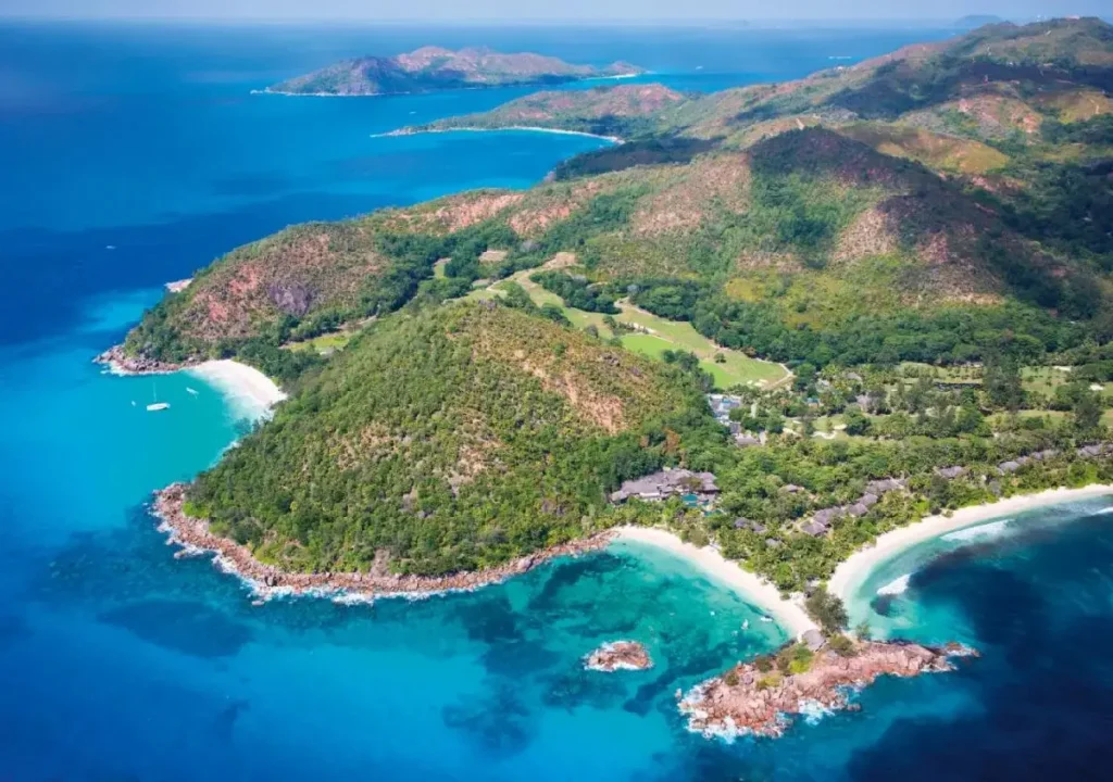Aerial view of a tropical island with lush green hills and turquoise waters, featuring sandy beaches and a serene coastline.