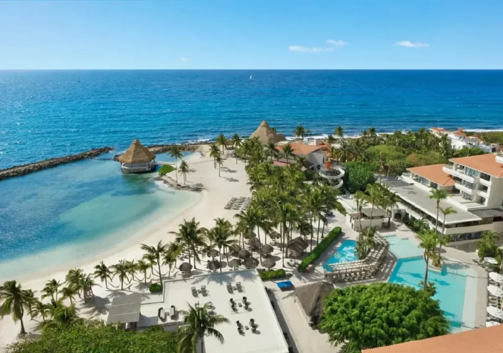 Stunning beach resort with clear blue waters, palm trees, and a pool, perfect for a tropical getaway.