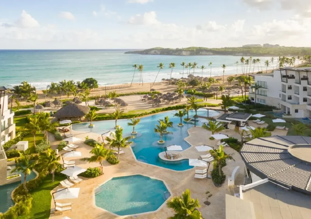 Tropical resort with swimming pools and ocean views, surrounded by palm trees and sandy beach, perfect for relaxation.