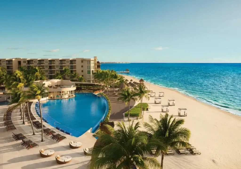 Luxurious beachfront resort with a stunning pool, palm trees, and inviting sun loungers by the azure ocean.