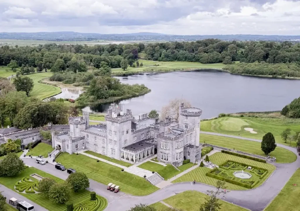 Aerial view of a majestic castle surrounded by lush greenery and a serene lake, showcasing beautiful landscaped gardens.