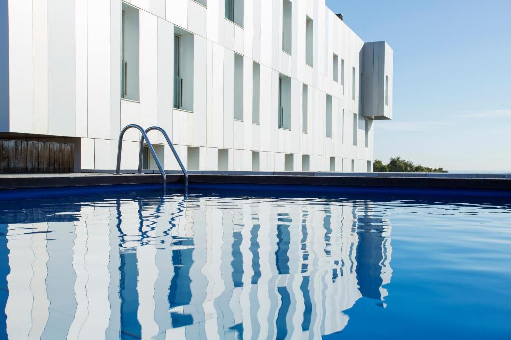 Modern swimming pool with a sleek design, reflecting a contemporary building against a clear blue sky.