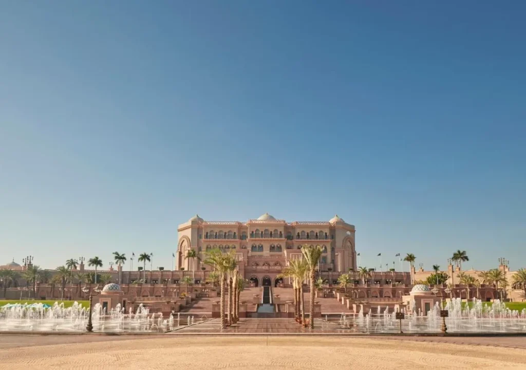Stunning view of a grand palace with palm trees and fountains under a clear blue sky. Perfect for luxury travel inspiration.