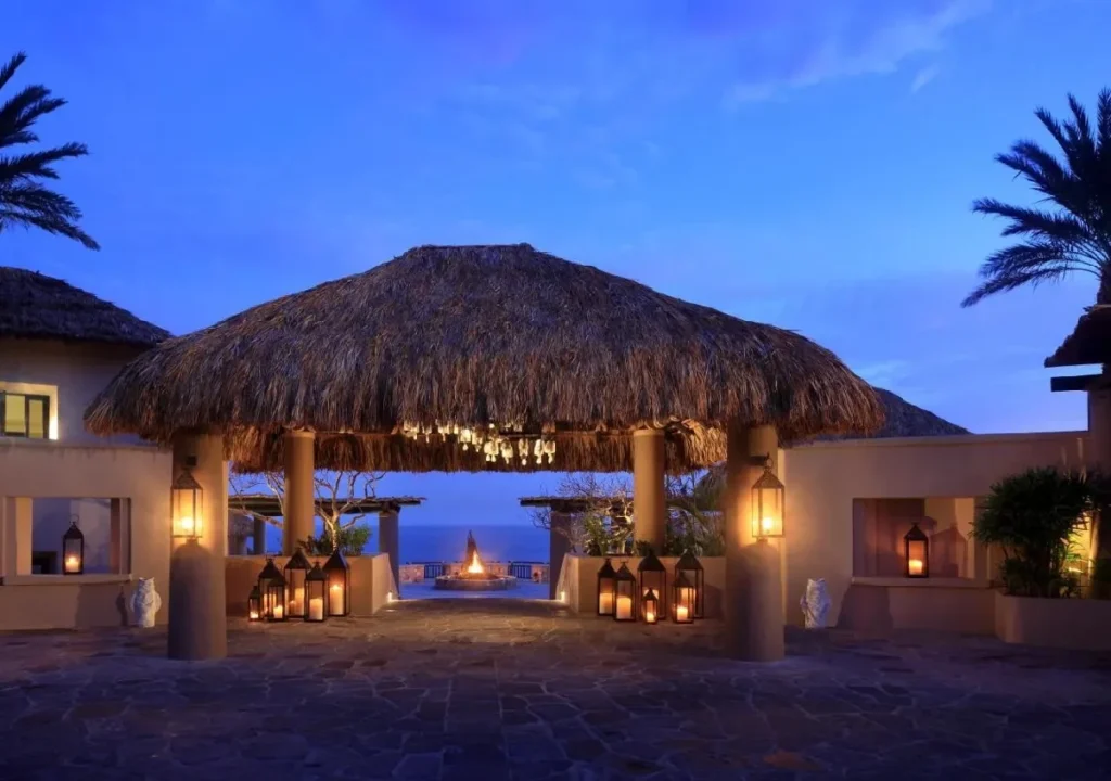 Tropical resort entrance at twilight, featuring a thatched roof and glowing lanterns, creating a welcoming ambiance.