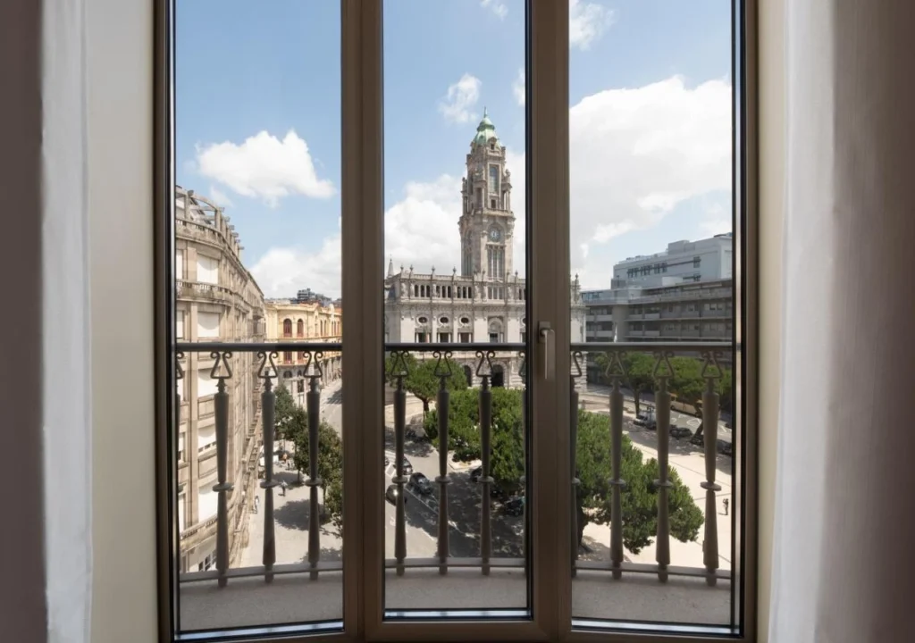 View from a balcony showing a cityscape with historic architecture and trees under a bright blue sky in Porto.
