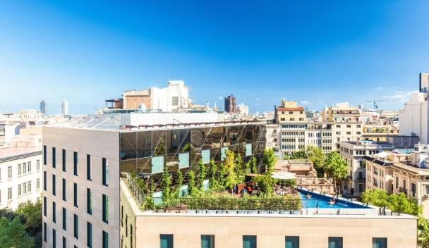 Modern rooftop garden with pool overlooking Barcelona’s skyline under a clear blue sky.