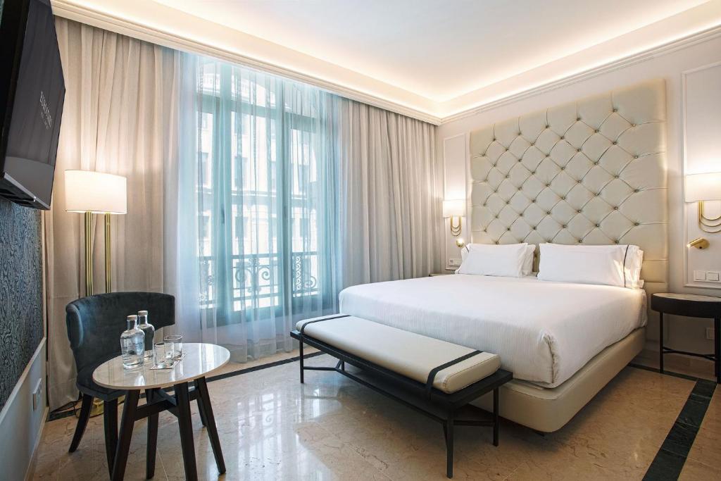 Luxurious hotel room featuring a king-size bed, elegant decor, and natural light from large windows.