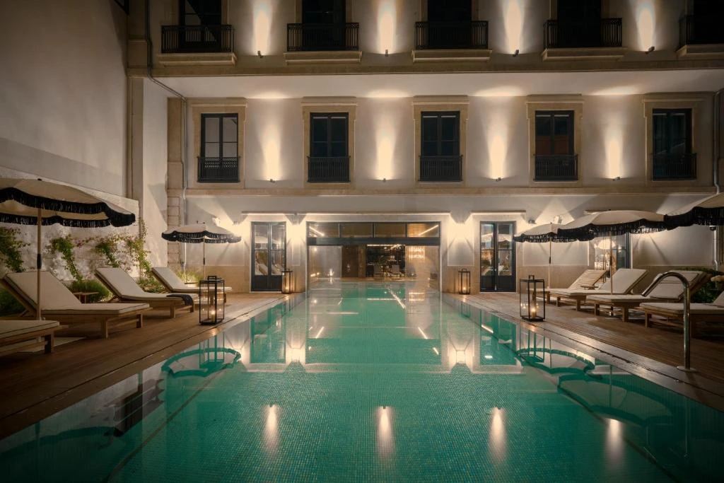Luxurious hotel poolside at night, featuring loungers, umbrellas, and elegant lighting reflecting on the water.