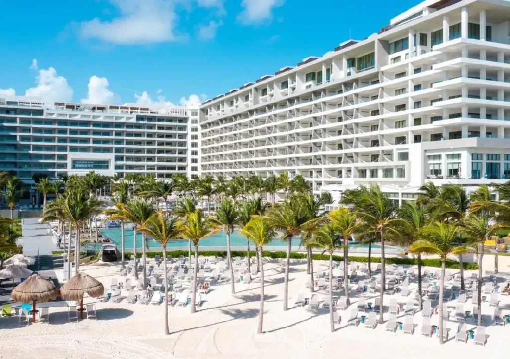 Stunning beachfront resort with white sand, palm trees, and a luxurious pool area under a bright blue sky.