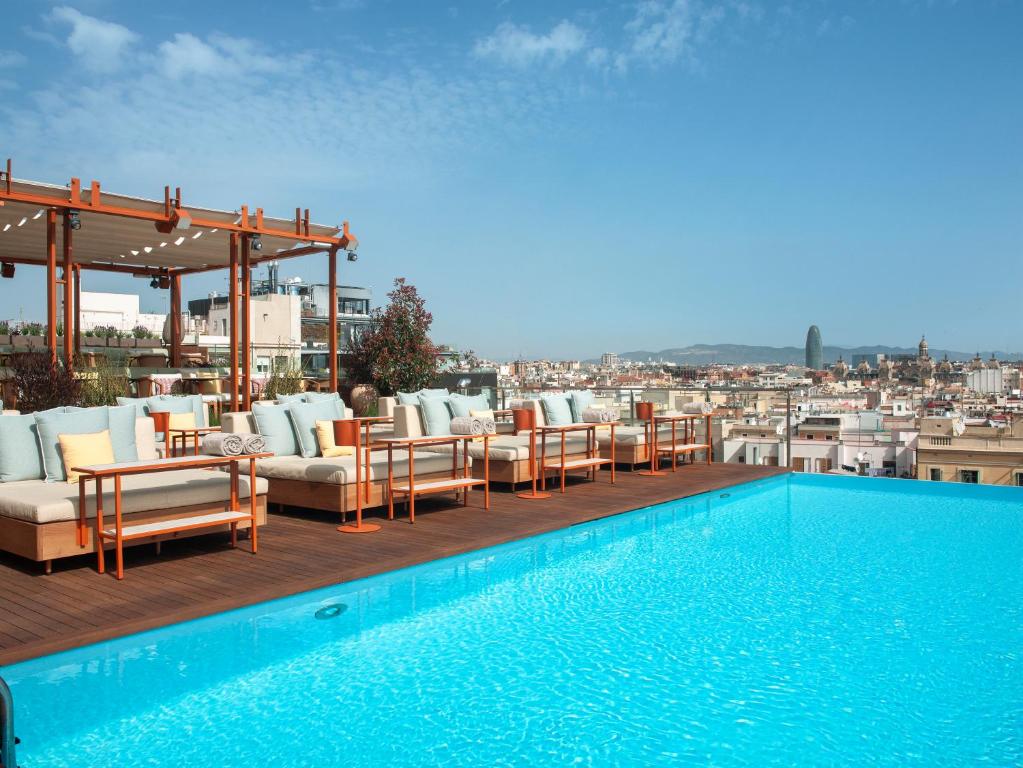 Stylish rooftop pool and lounge area overlooking a vibrant cityscape under a clear blue sky. Perfect for relaxation.