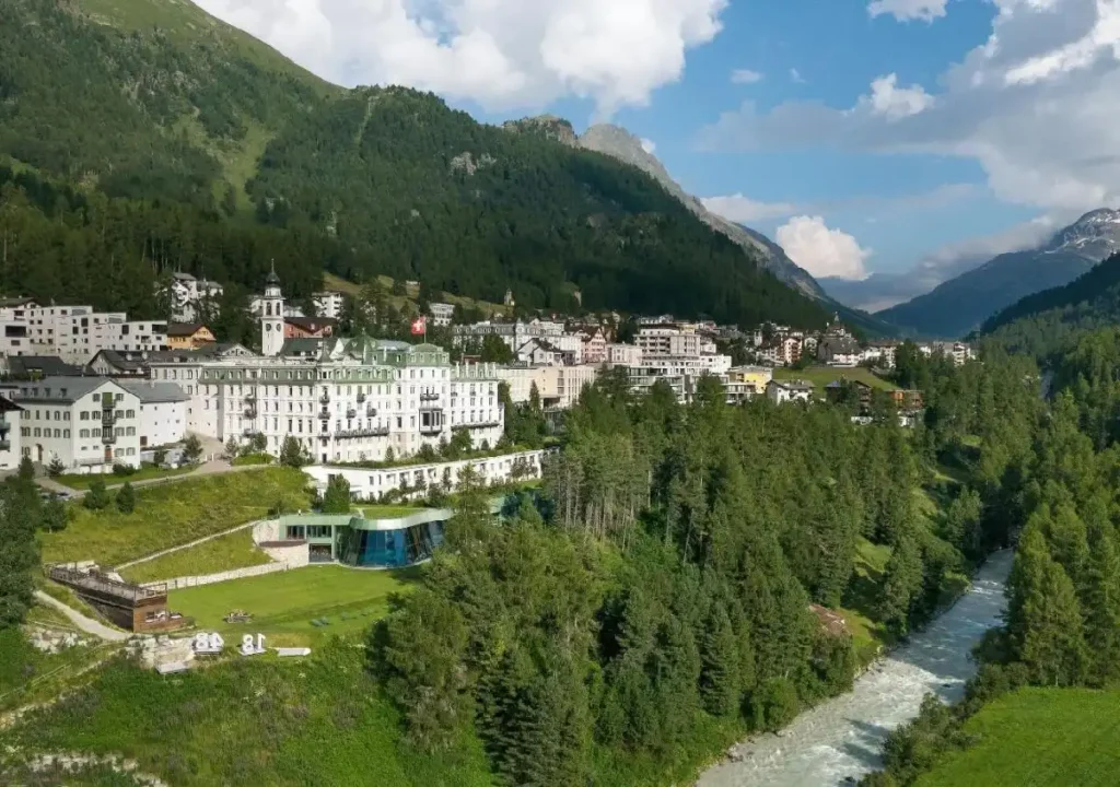 Scenic view of a resort town nestled in the Swiss Alps, surrounded by lush greenery and a flowing river.