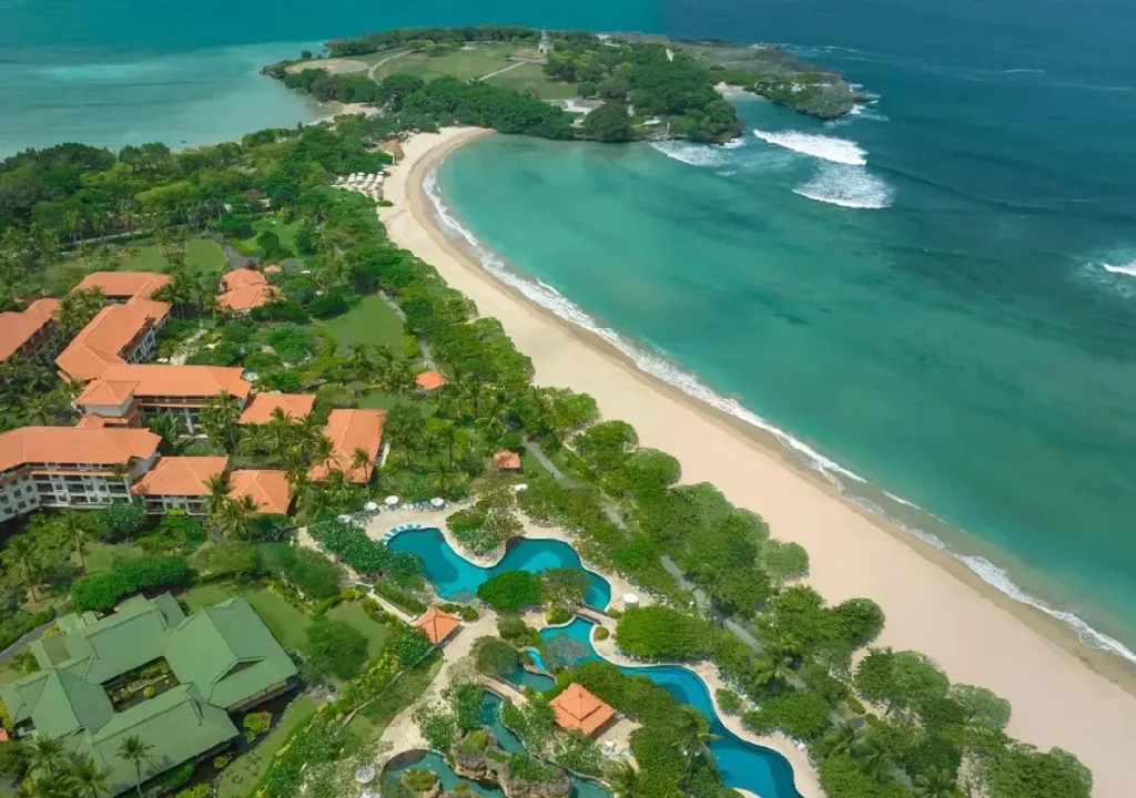 Aerial view of a tropical resort with sandy beach, lush greenery, and crystal-clear waters, perfect for relaxation.