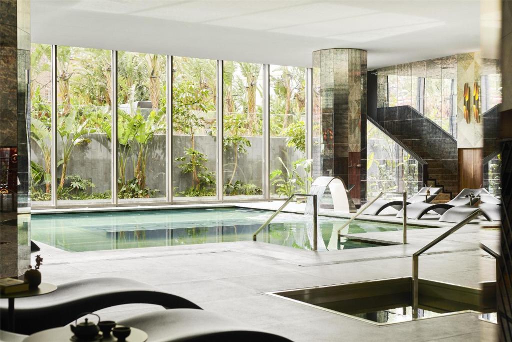 Luxurious indoor spa with a serene pool, cozy lounge chairs, and lush greenery visible through large glass windows.