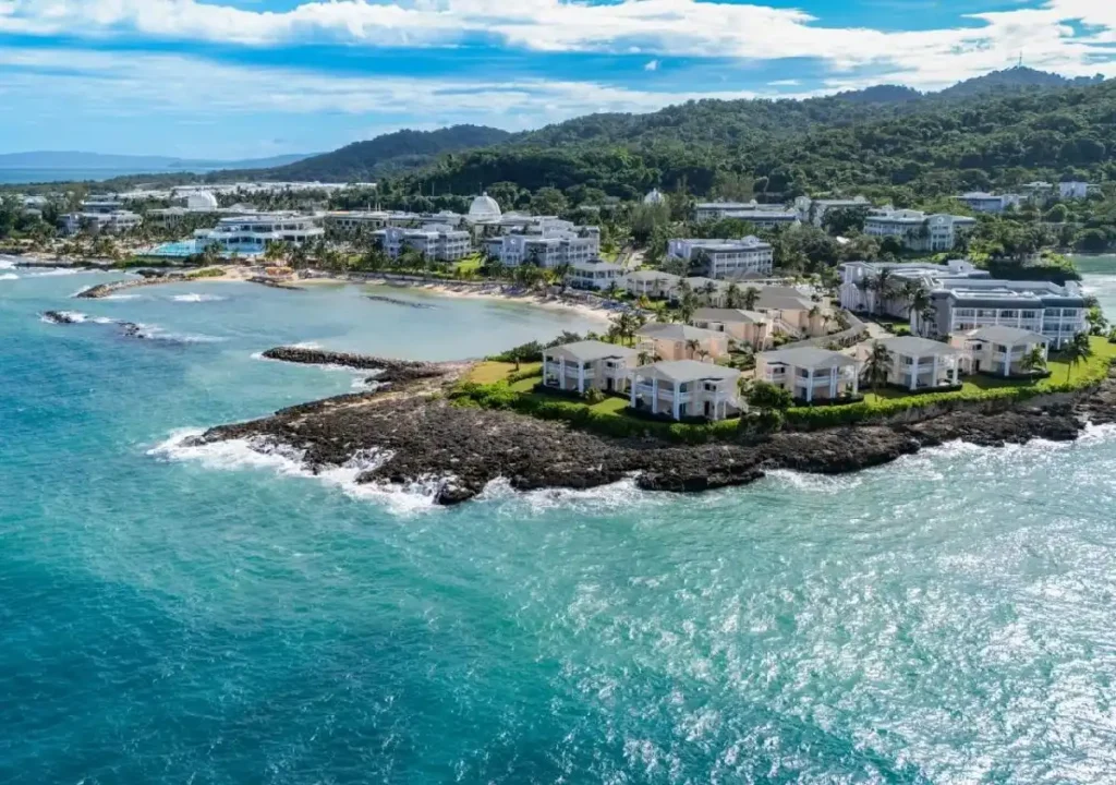Scenic aerial view of coastal resort with lush greenery, turquoise waters, and sandy beaches under a blue sky.