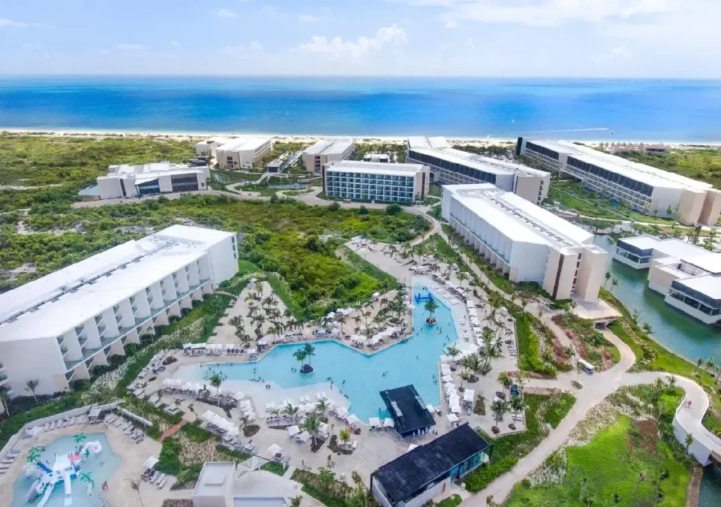 Aerial view of a luxury resort with pools and ocean in the background, surrounded by lush greenery. Perfect for a getaway.