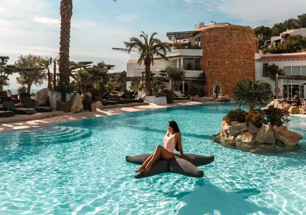 Woman relaxing on a star-shaped float in a luxurious pool surrounded by palm trees and modern architecture.