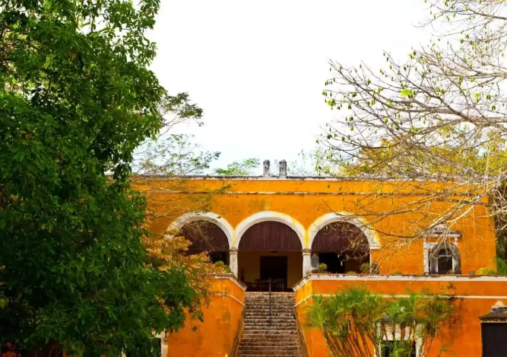 Stunning yellow historic building framed by lush greenery and trees, showcasing beautiful architectural arches.