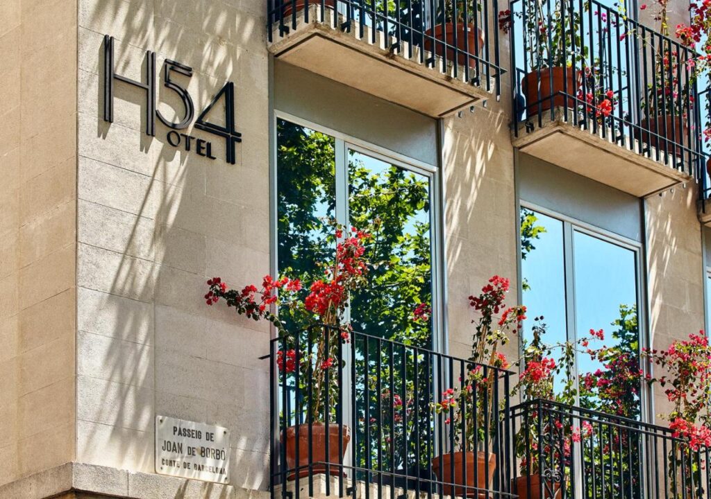 Exterior view of H54 Hotel showcasing elegant balconies adorned with vibrant flowers and reflective glass windows.