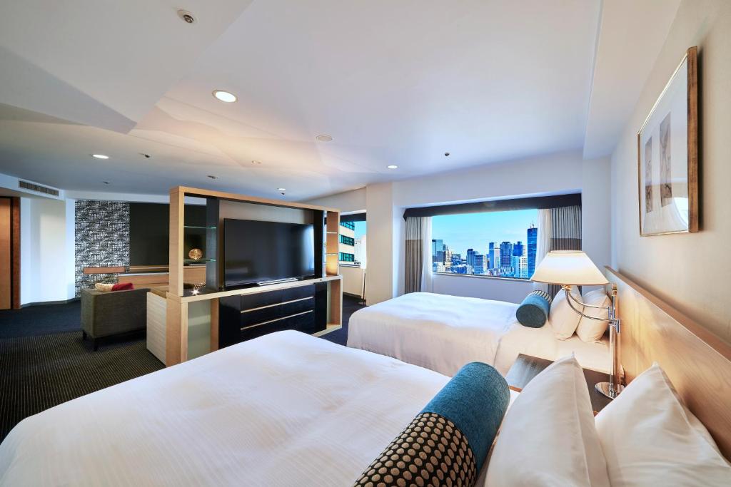 Modern hotel room featuring two beds, a TV, cozy seating, and a city skyline view from large windows. Perfect for travelers.