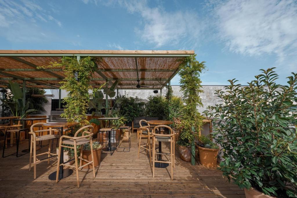 Rooftop garden lounge with wooden flooring, greenery, and stylish seating under a woven canopy against a blue sky.