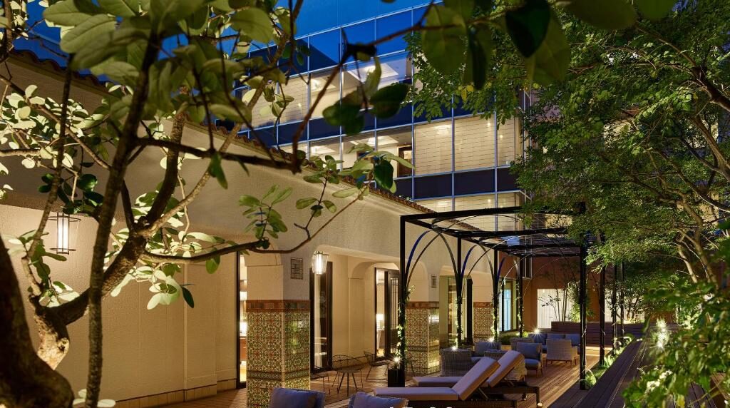 Stylish outdoor lounge area with check-in at 15:00 and check-out at 12:00, surrounded by greenery and modern architecture.