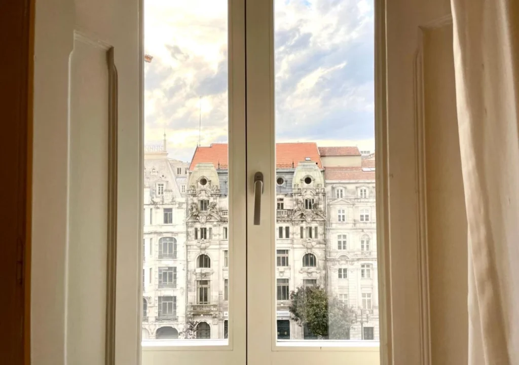 View through a window showcasing elegant historic architecture and a cloudy sky.