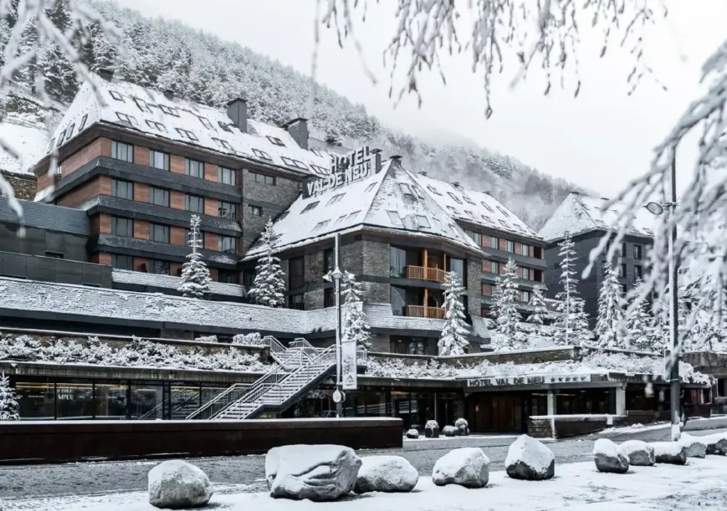 Hotel Val de Neu surrounded by snow-covered trees and mountains in a picturesque winter landscape.
