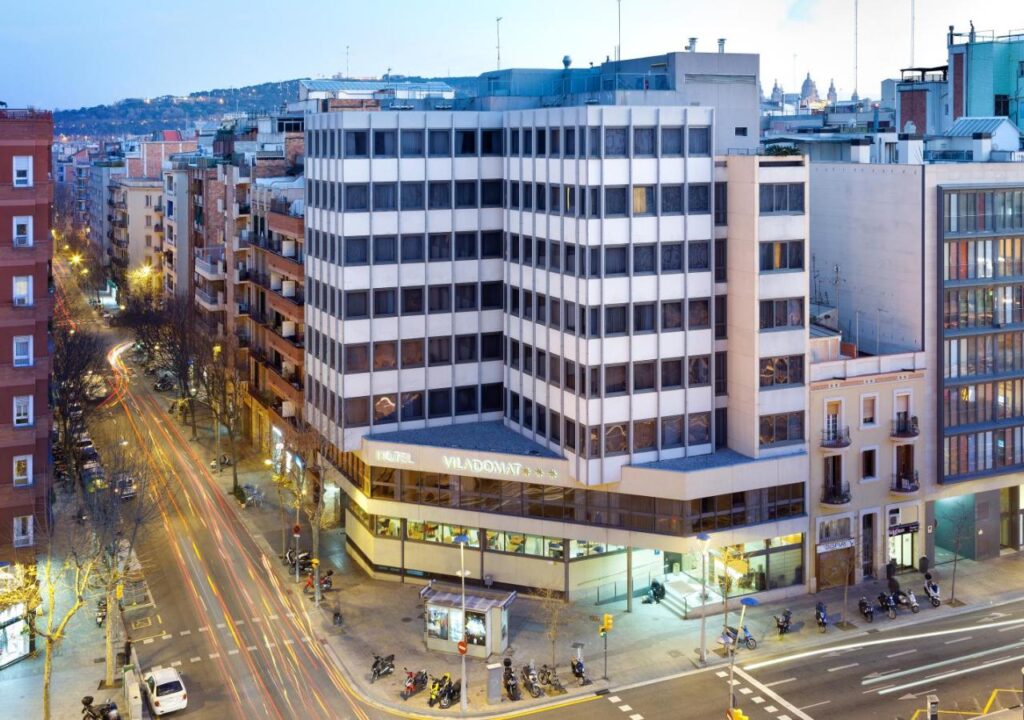 View of Hotel Viladomat with city streets and traffic at dusk in Barcelona, showcasing modern urban architecture.