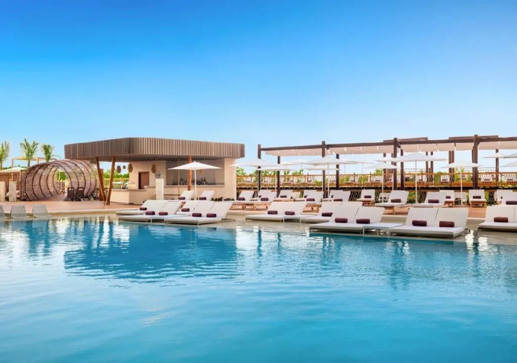 Stylish poolside lounge area with sunbeds and modern bar, perfect for relaxation under a clear blue sky.
