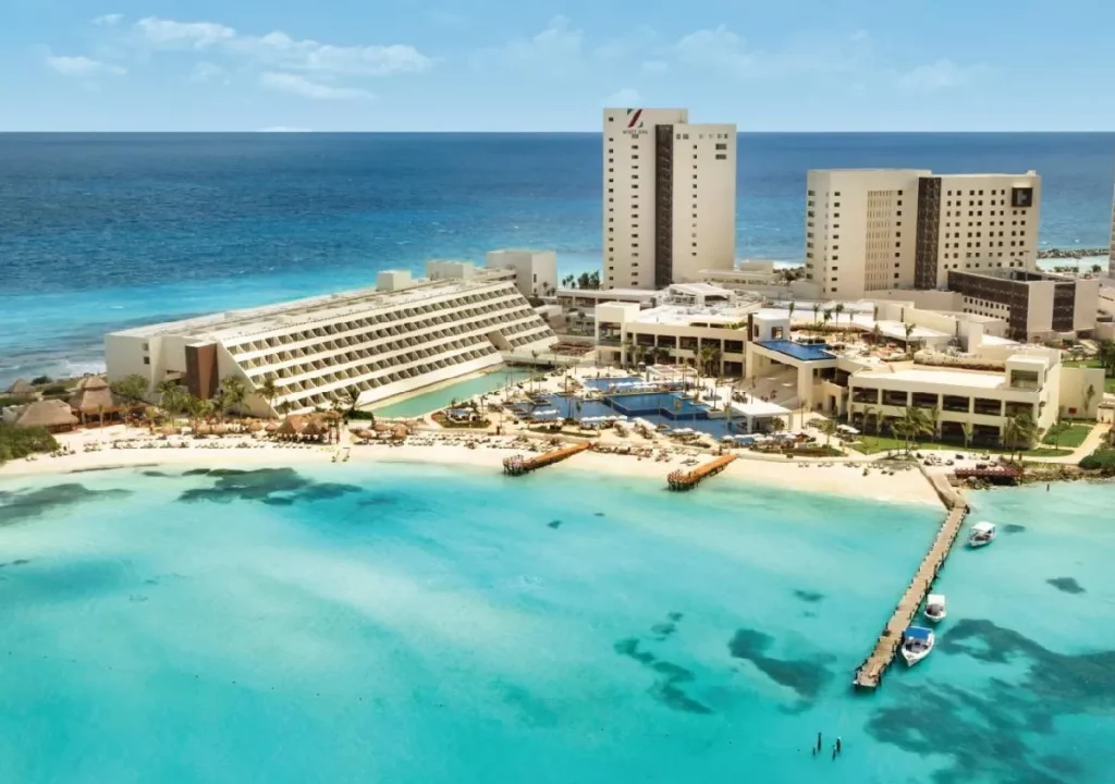 Luxurious beachfront hotel in Cancun with crystal-clear waters, pools, and sun loungers for a perfect tropical getaway.
