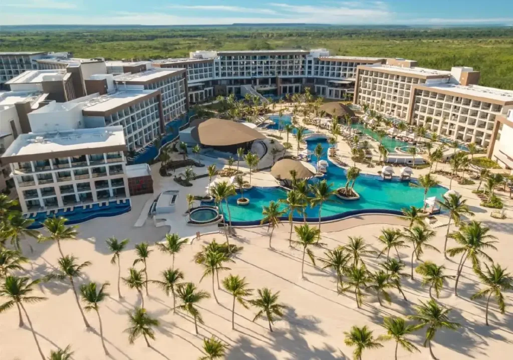 Aerial view of a luxurious resort featuring pools, lush palm trees, and modern architecture in a tropical setting.