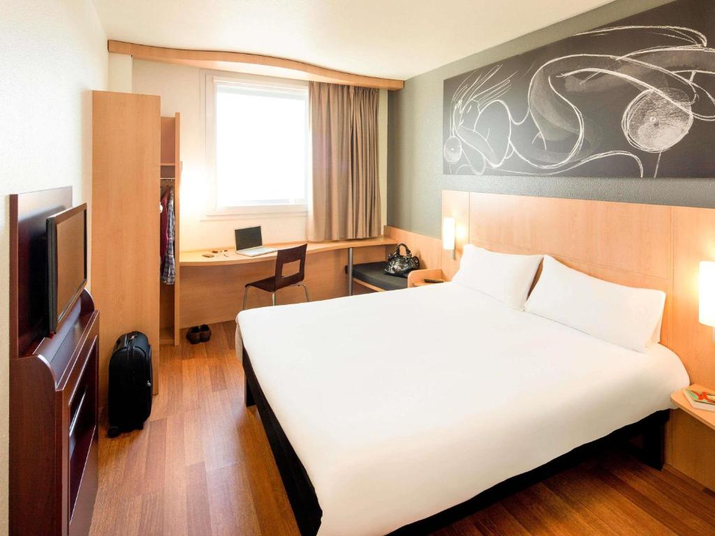 Modern hotel room featuring a double bed, desk, and wardrobe with a minimalist design and warm wood accents.