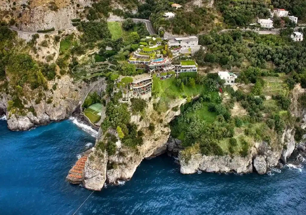 Aerial view of stunning coastal cliffs featuring a luxurious hotel and lush greenery overlooking the blue sea.