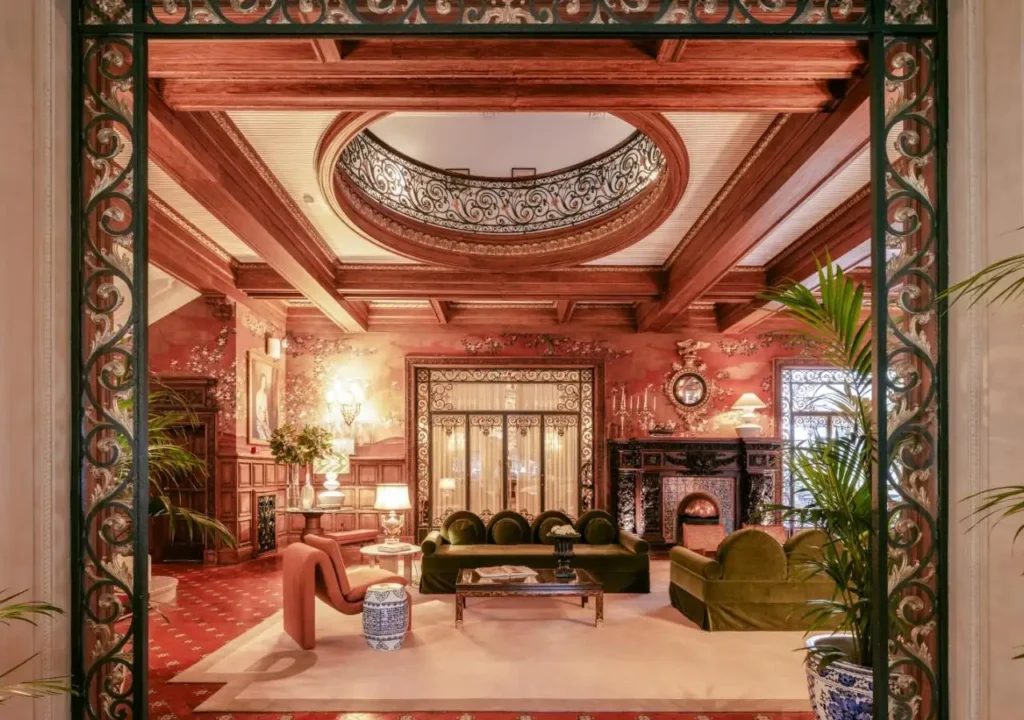 Elegant vintage living room with ornate decor, plush seating, and floral wallpaper, framed by intricate ironwork.