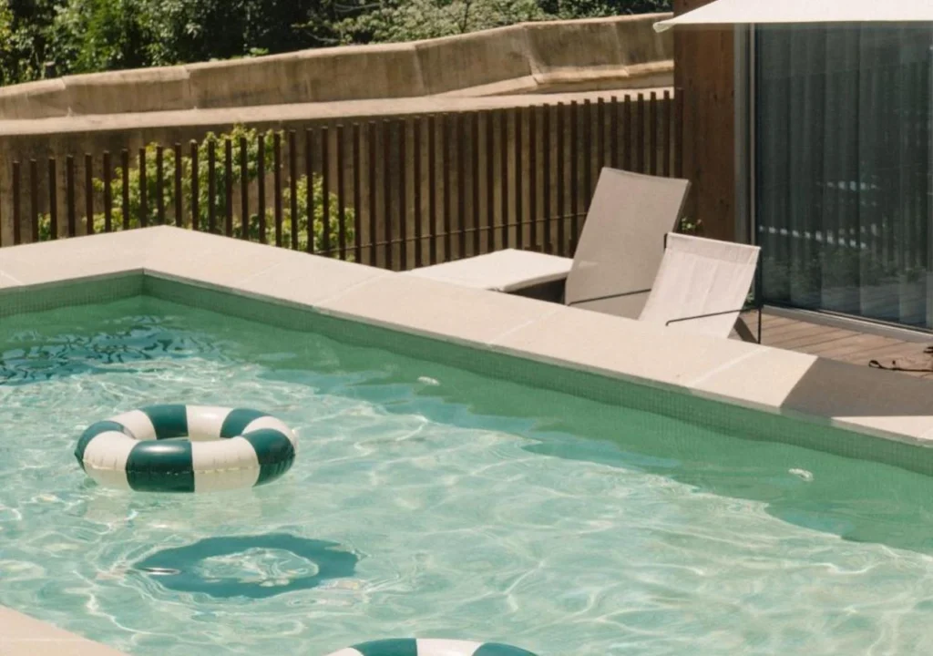 Tranquil swimming pool with inflatable rings, surrounded by lush greenery and a sunlit deck chair for relaxation.