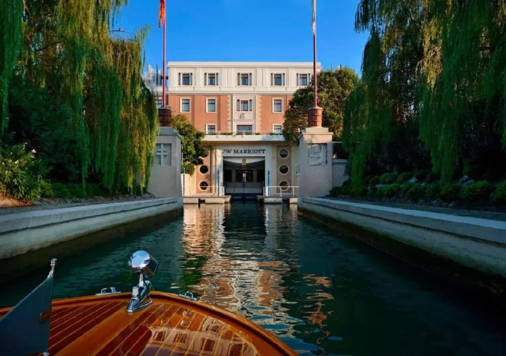 View of the JW Marriott hotel from a boat, surrounded by lush greenery and reflections on the water.