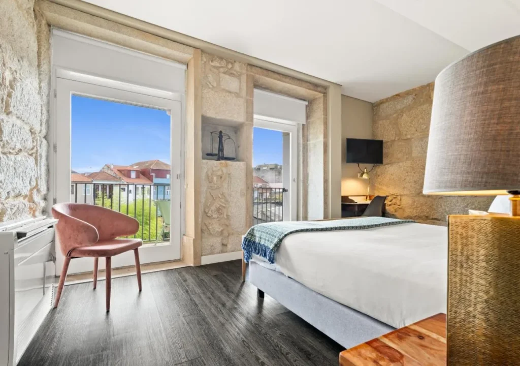 Cozy hotel room with wooden flooring, stone walls, and large windows offering a view of the outdoors.