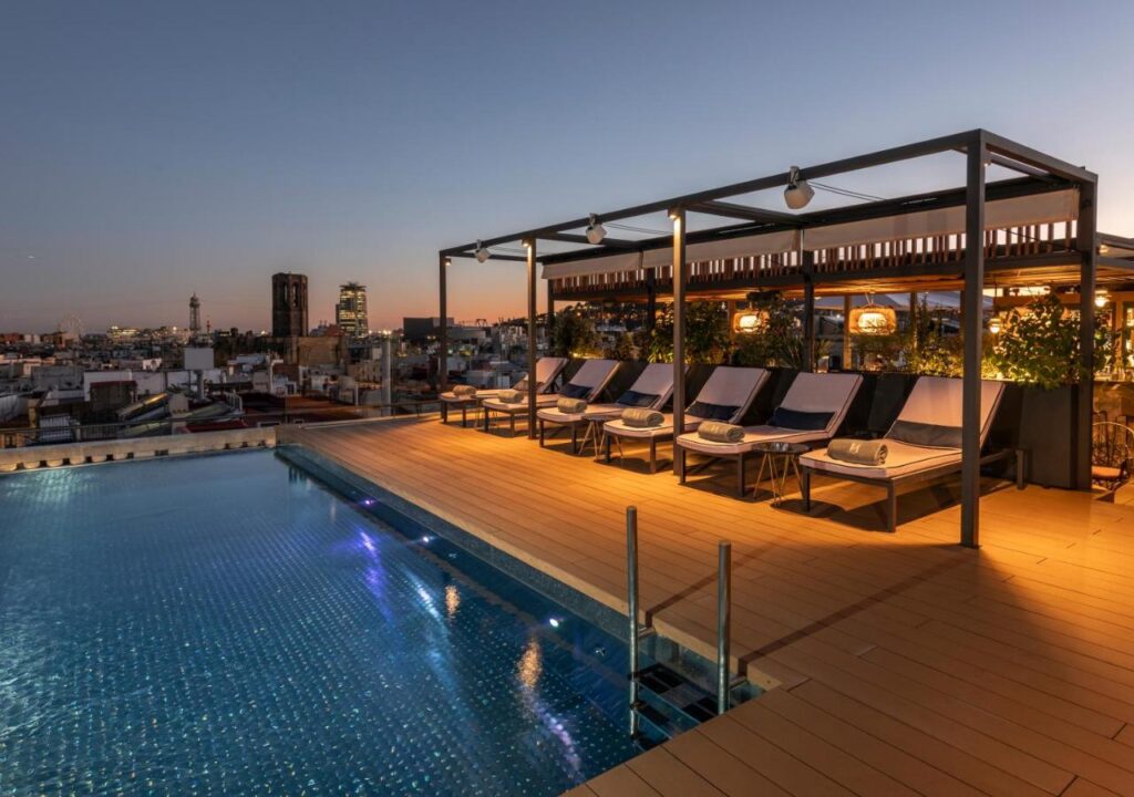 Rooftop pool area at sunset with lounge chairs and city skyline views, perfect for relaxation and evening gatherings.
