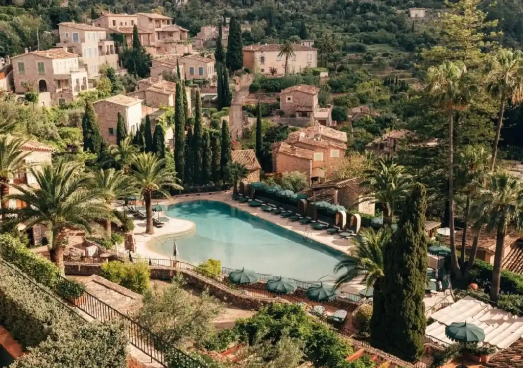 Aerial view of a serene pool surrounded by lush greenery and rustic stone houses in a picturesque landscape.