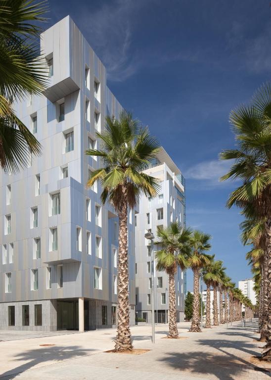 Modern building facade with palm trees along the sidewalk under a clear blue sky, showcasing contemporary architecture.