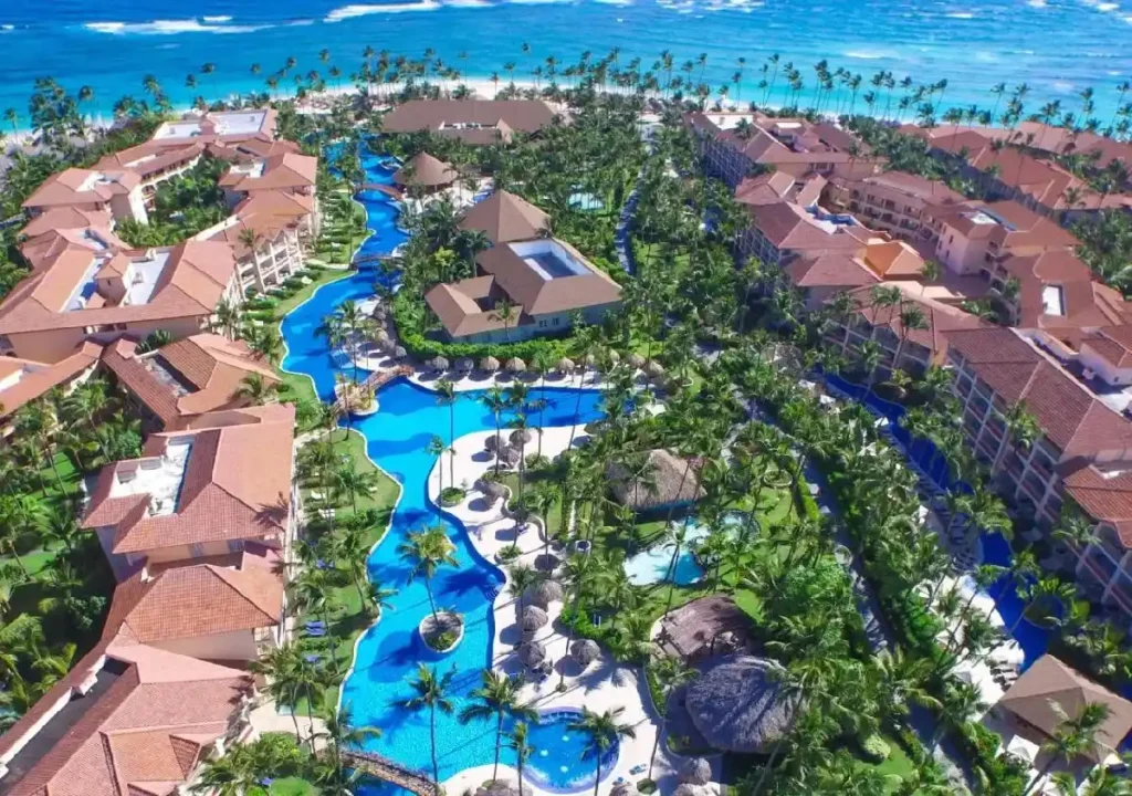 Luxurious resort overlooking tropical pools and ocean, surrounded by lush greenery and palm trees. Perfect vacation destination.