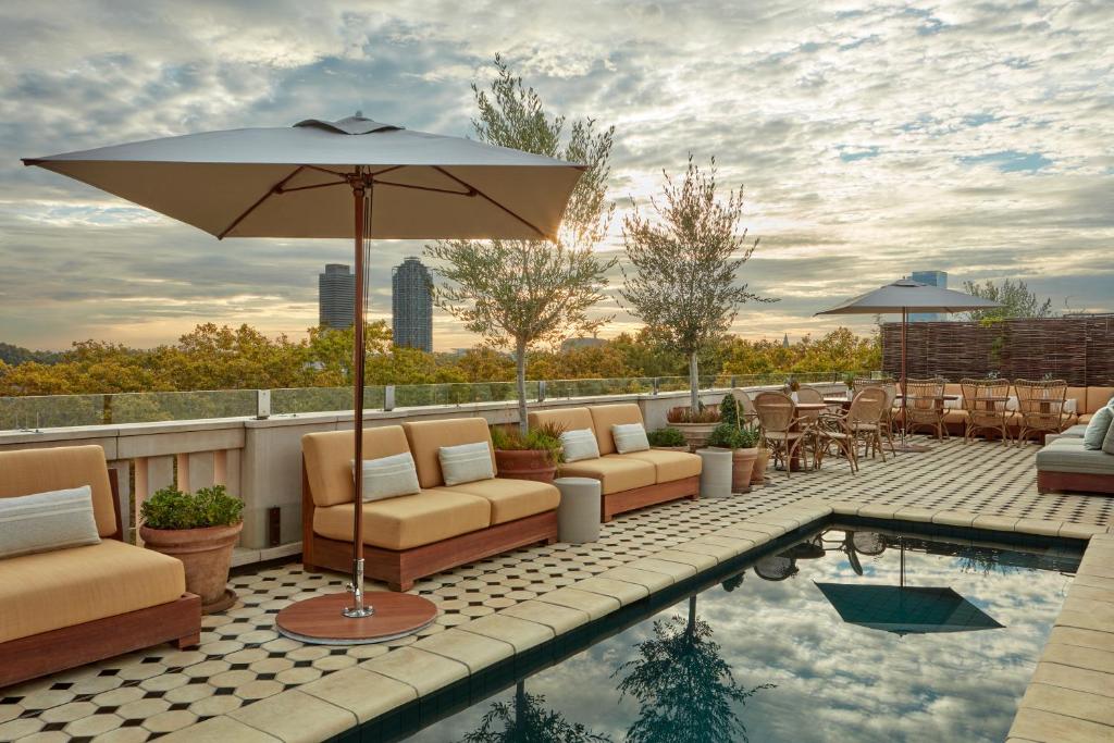 Rooftop pool area with modern seating, umbrellas, and stunning sunset views over cityscape and greenery.