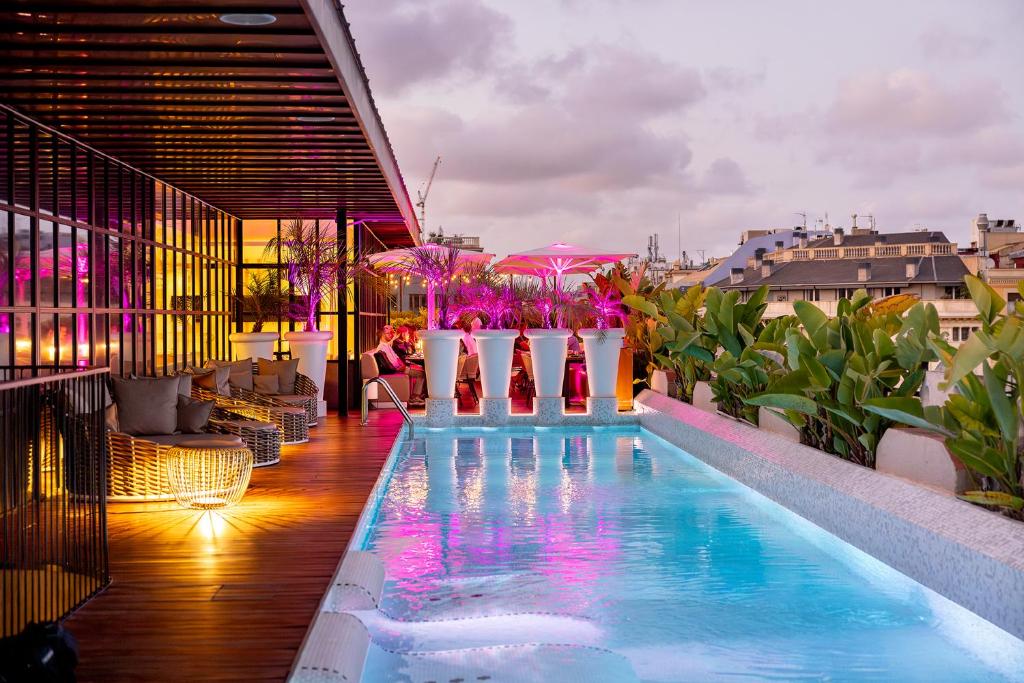 Rooftop pool area with vibrant lighting, modern seating, and lush plants, offering a stunning city view at sunset.