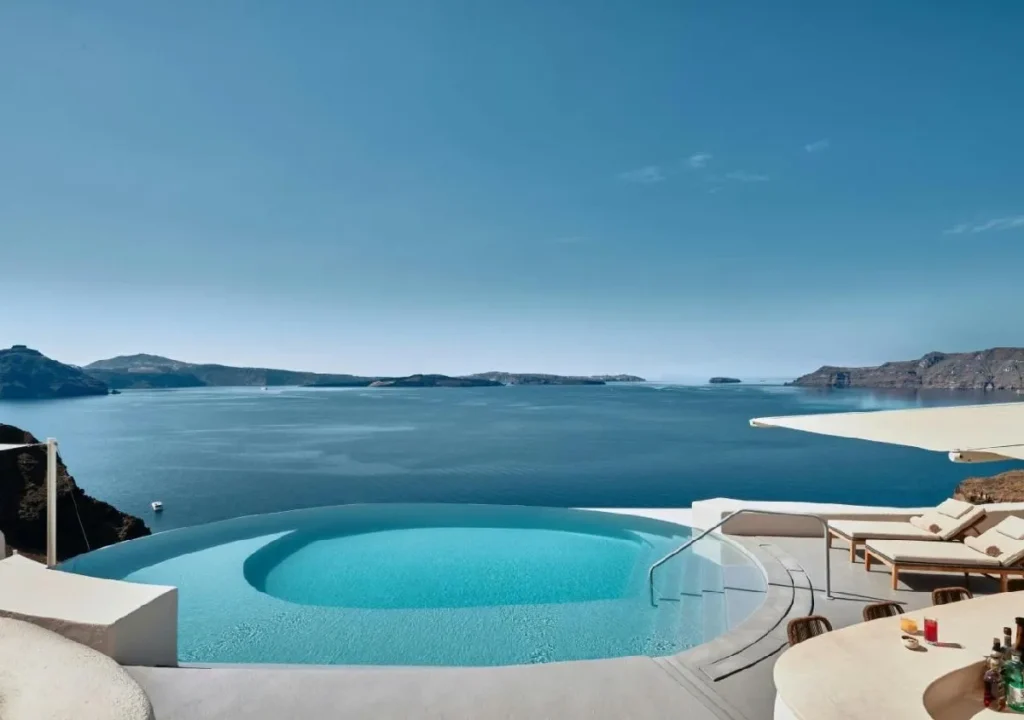 Stunning infinity pool overlooking the serene blue waters of Santorini, with scenic hills in the background.