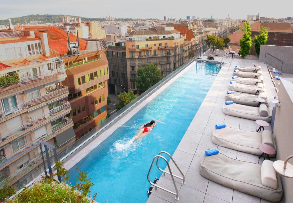 Rooftop pool with a swimmer, lounging chairs, and city skyline in the background, showcasing a relaxing urban retreat.